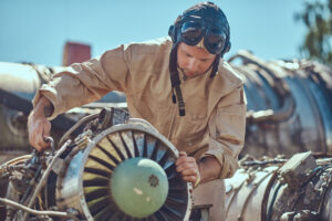 Portrait of a pilot-mechanic in uniform and flying helmet, repairing the dismantled airplane turbine in an open-air museum.