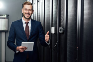 Selective focus of cheerful businessman holding digital tablet and showing thumb up in data center — Photo